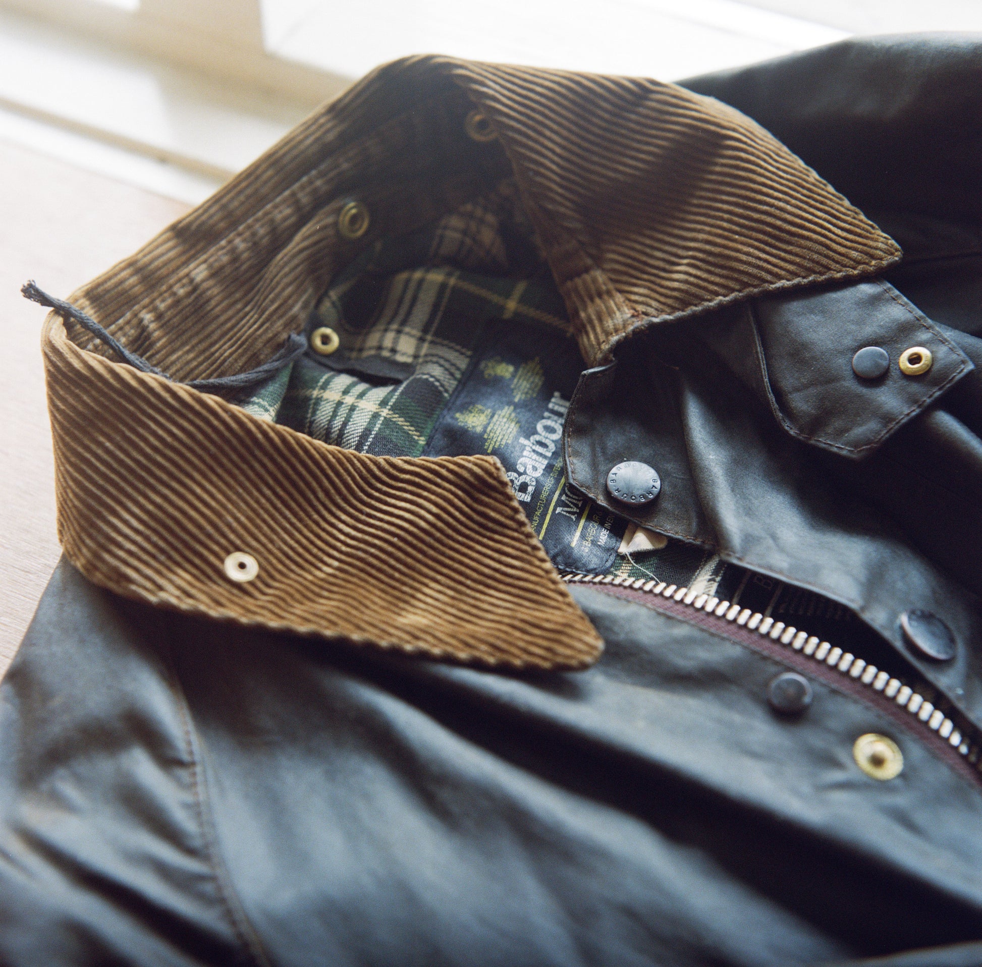 A green vintage Barbour waxed canvas jacket with a light brown corduroy collar.