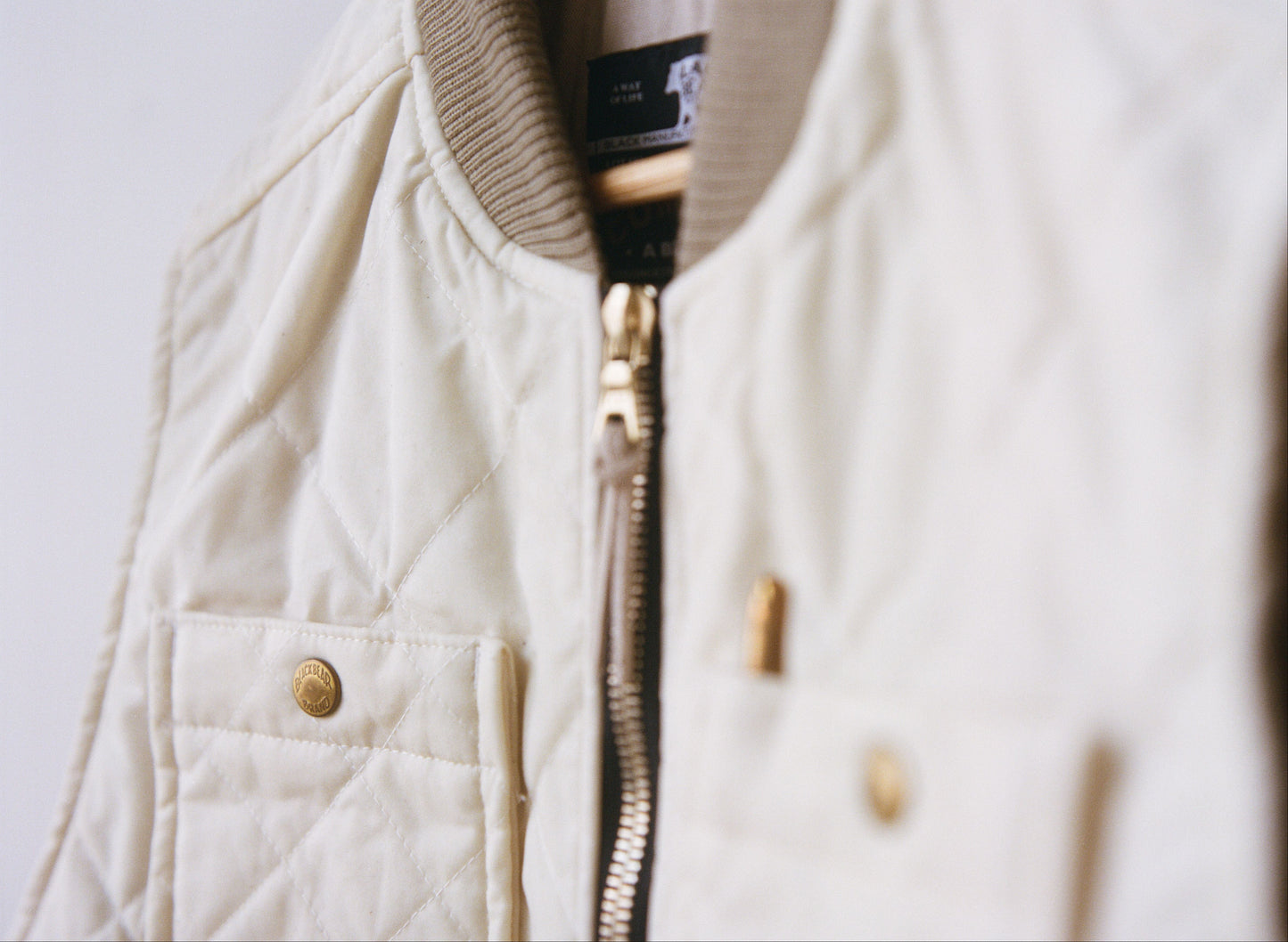A white quilted vest with brass buttons and a light brown collar. The foreground is blurry and the background of the image is sharp.