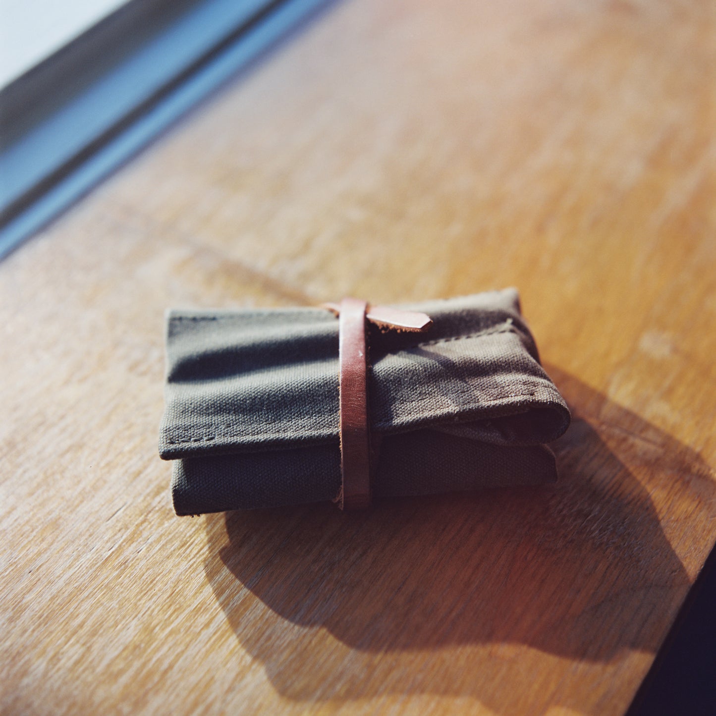 An image of a Bradley Mountain waxed canvas utility roll in Field Tan with a wooden background.