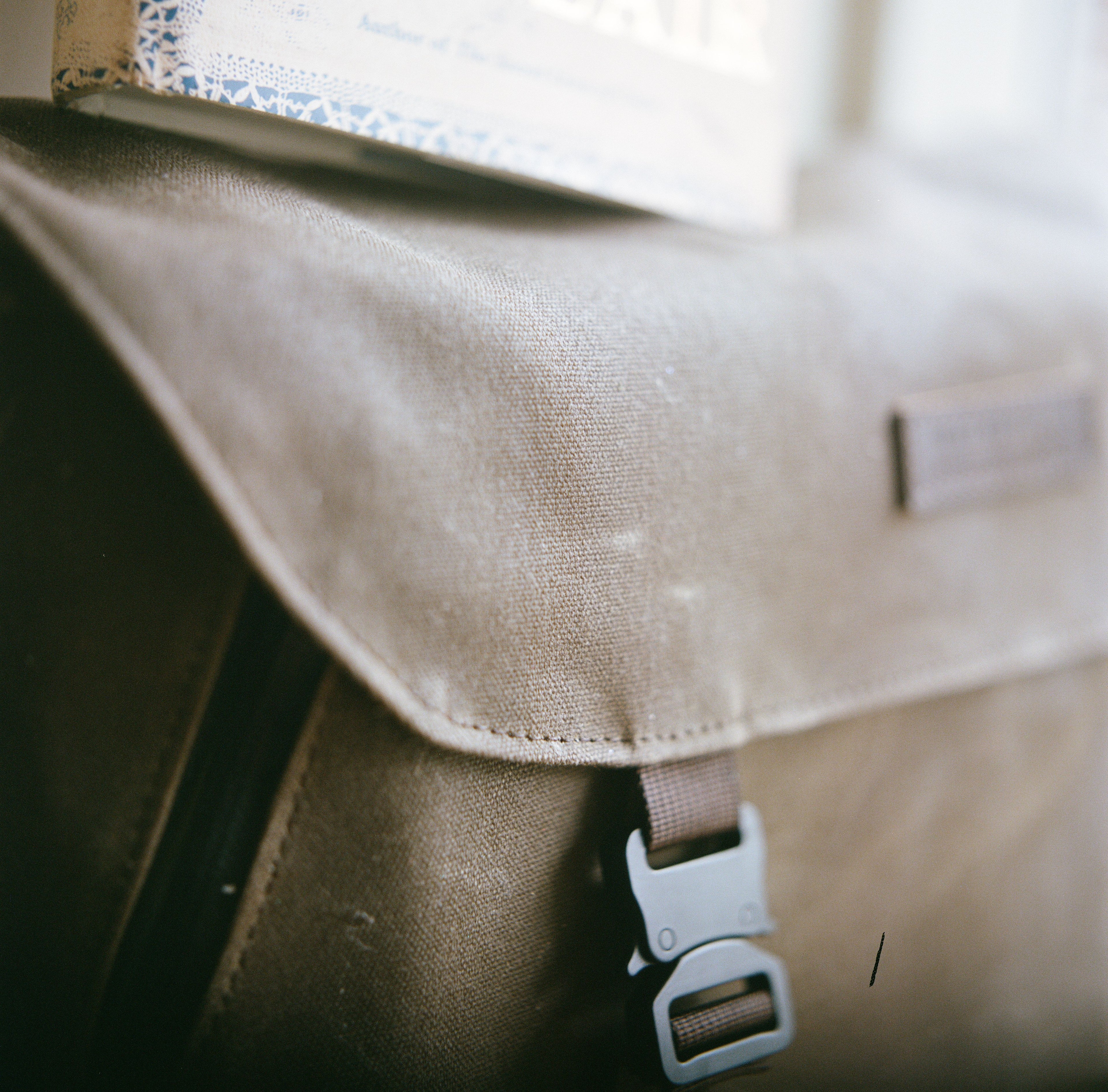 A Close-up image of a brown messenger bag made in America by Waterfield Designs with a paragliding buckle, blurred background.