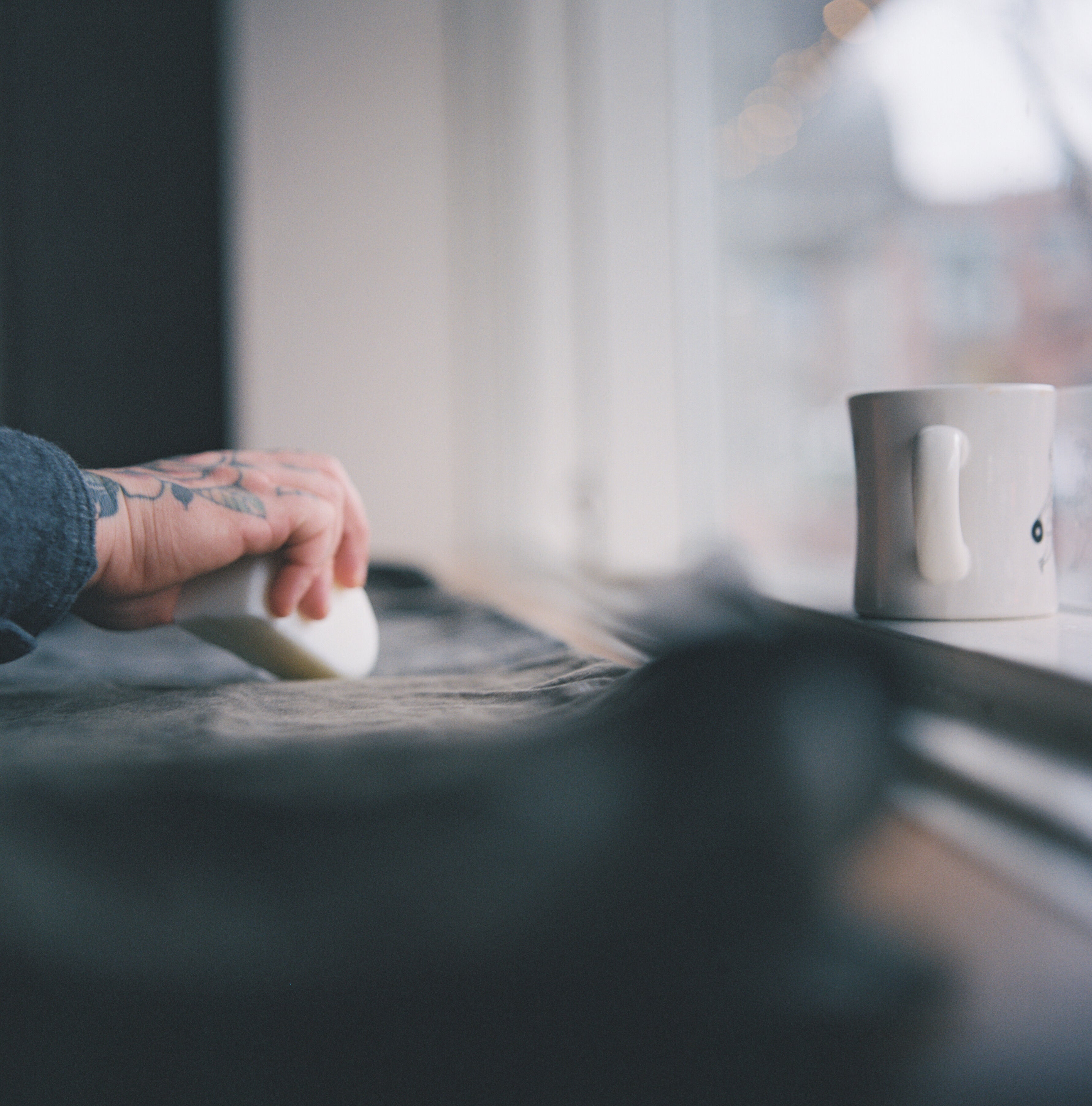 An image of a hand waxing canvas with a bar of wax. A coffee cup sits to the right.