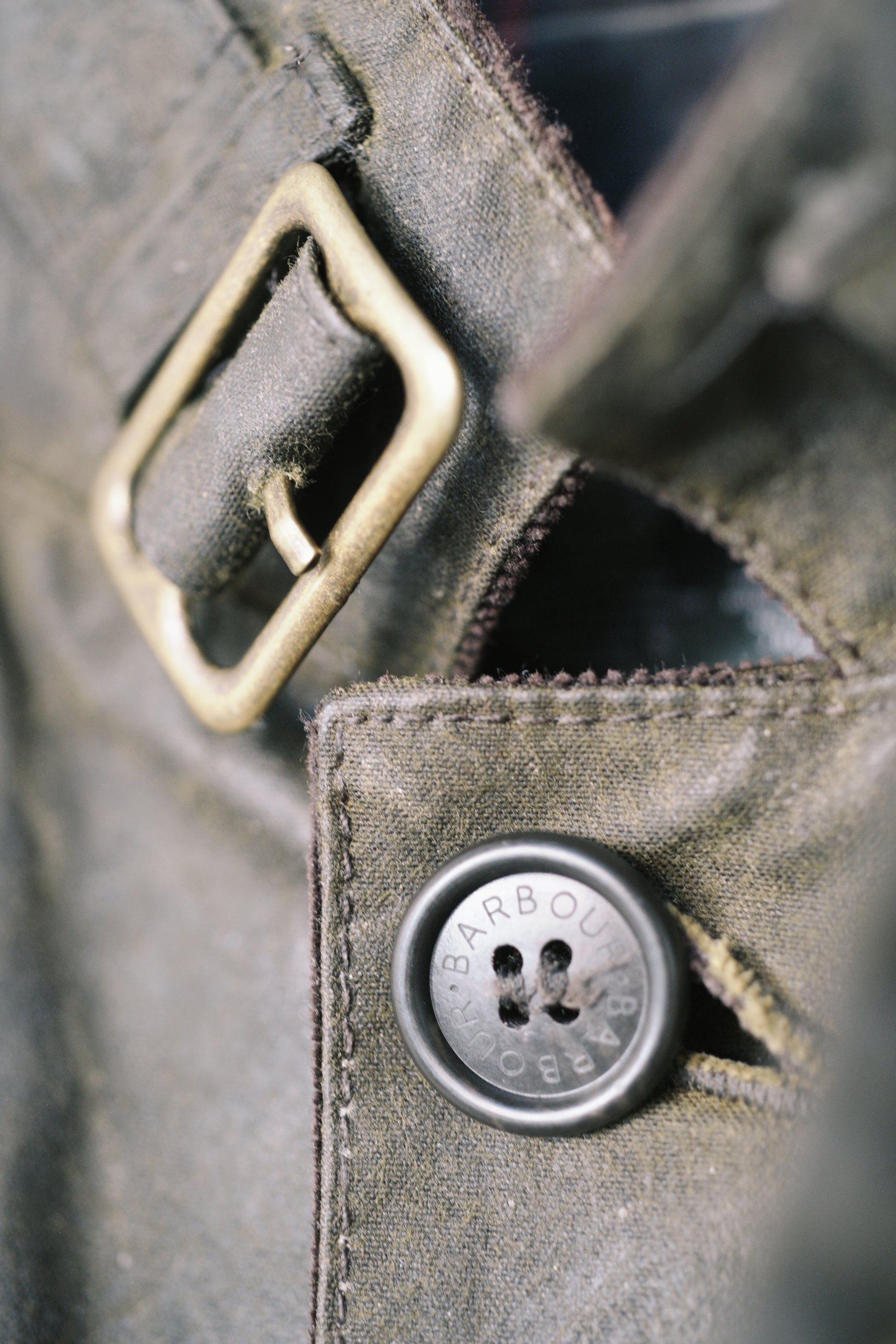 A close up image of a newly waxed canvas jacket collar with a perfectly aged brass buckle and button.