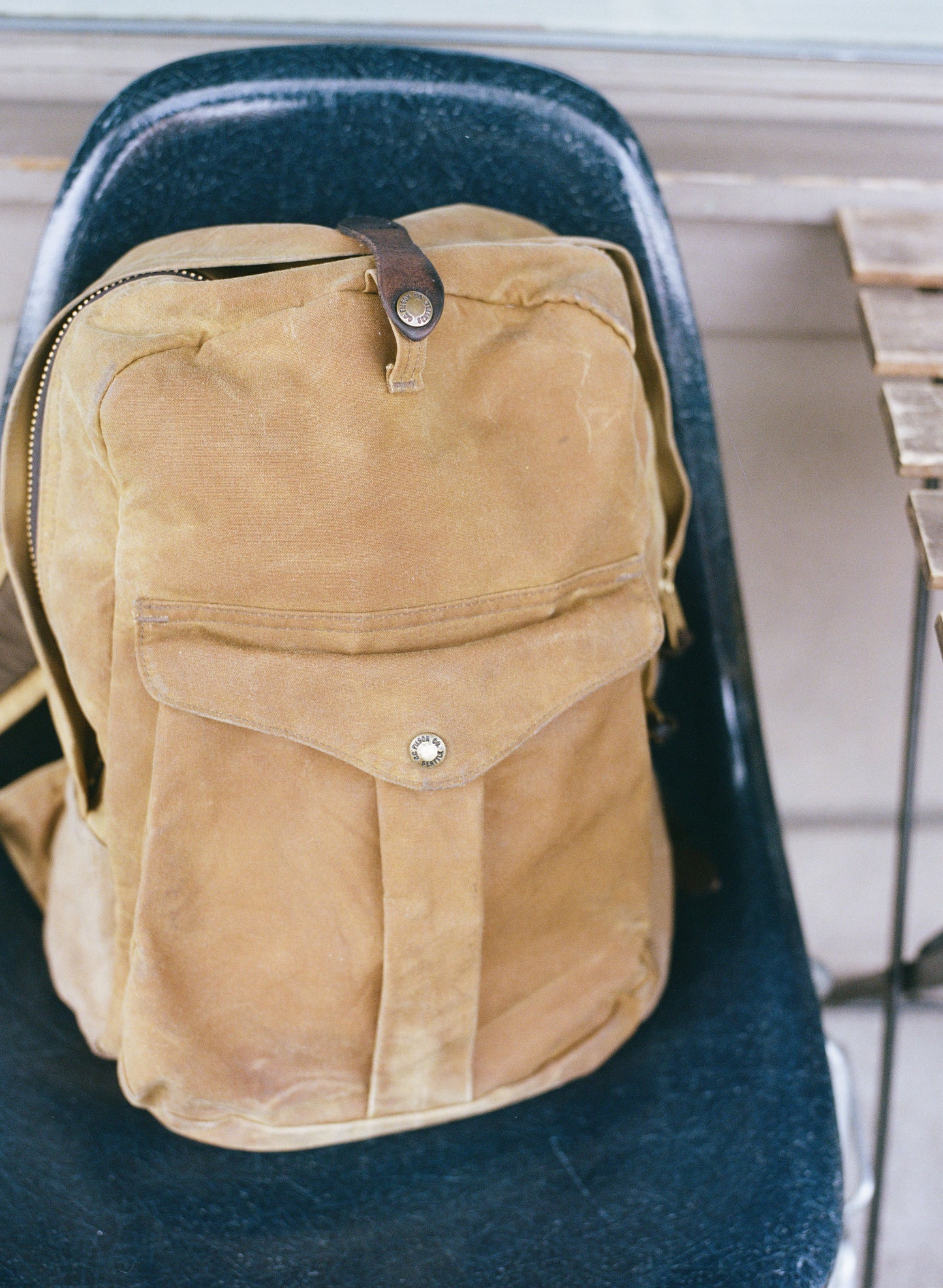 A brown waxed cavas backpack resting on a blue chair.