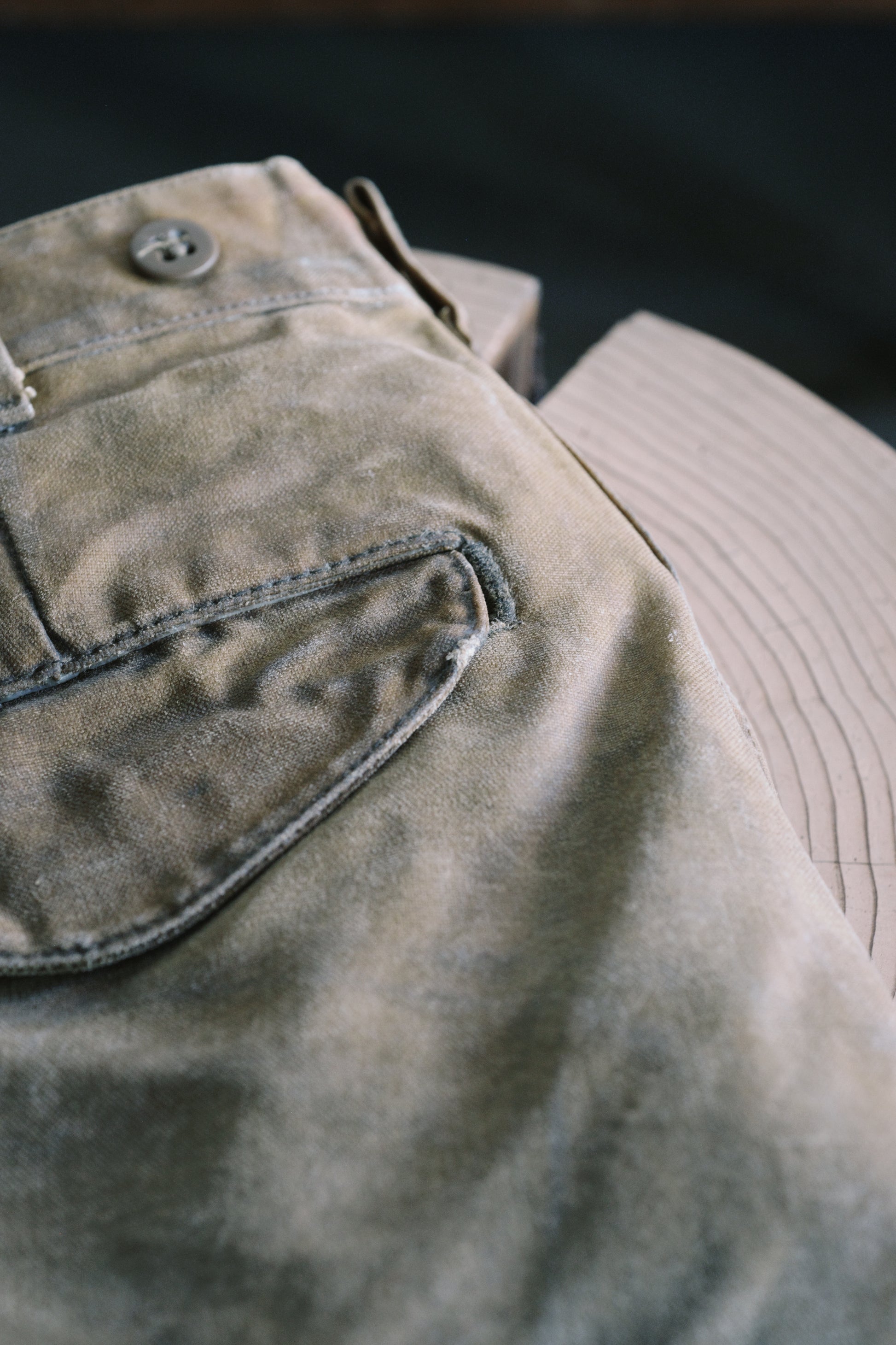 An image of Filson Tin Cloth pants with patina, with a wooden background.