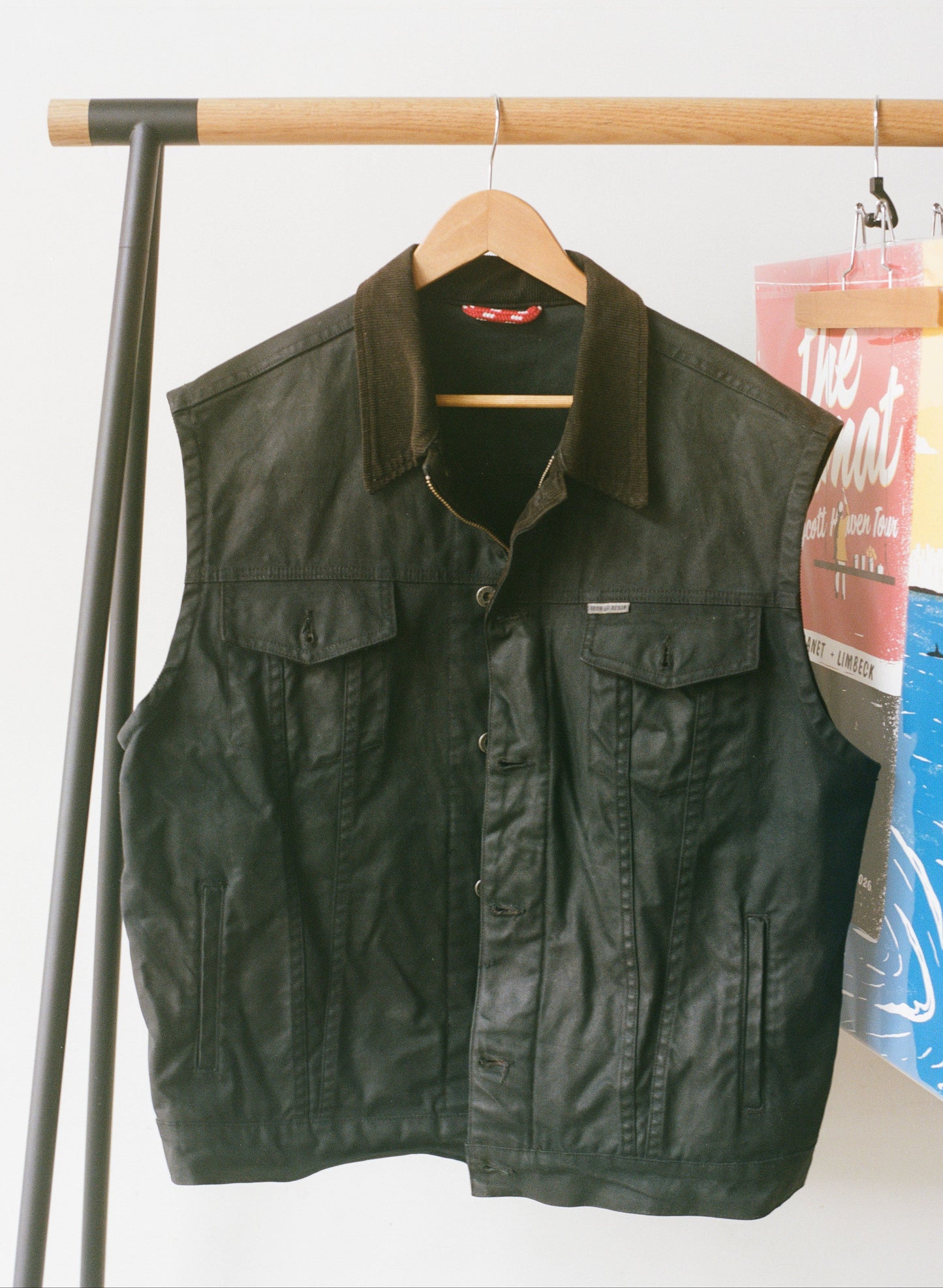 A black waxed canvas vest hanging up with a white background.