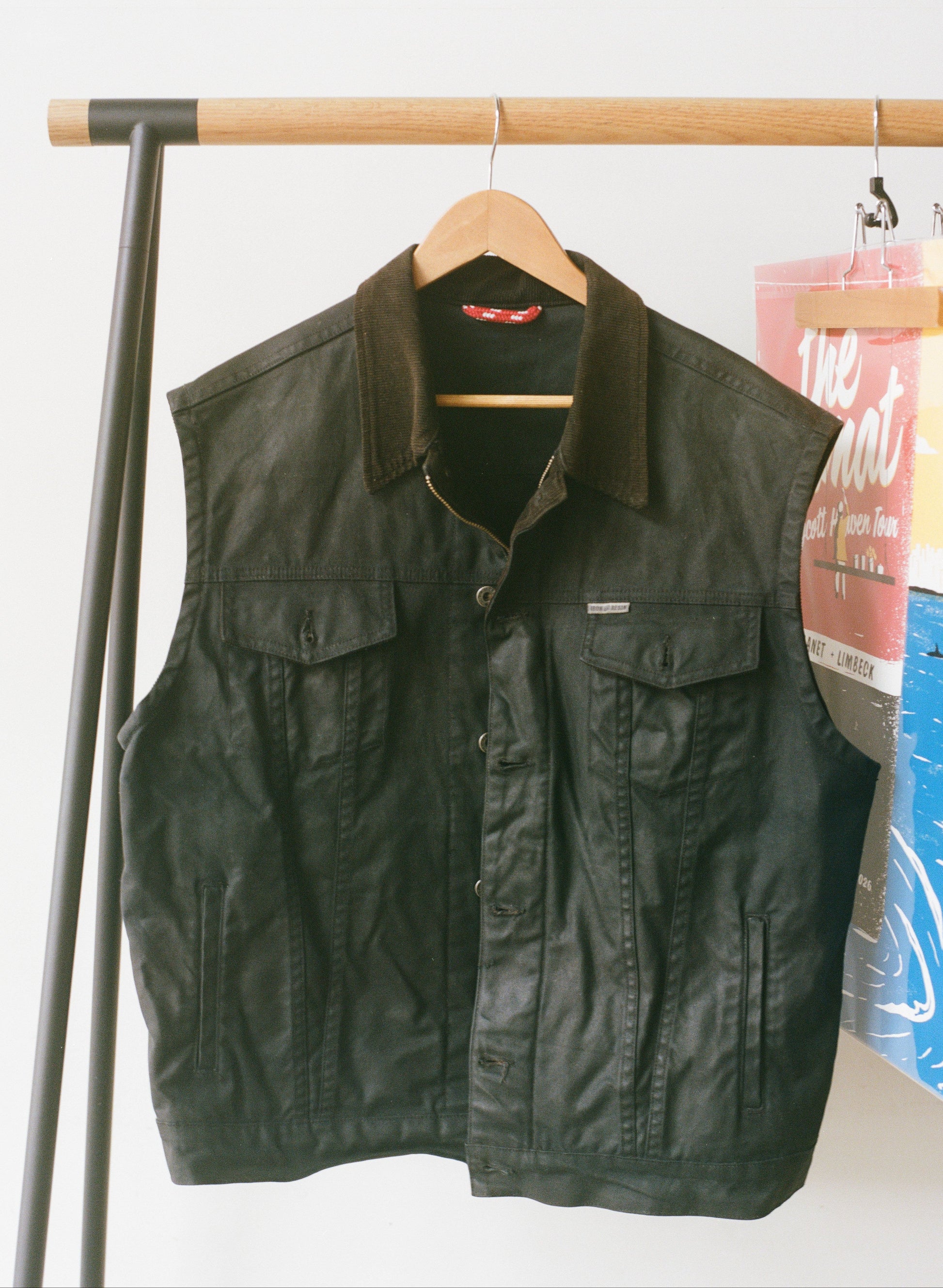 A black waxed canvas vest hanging up with a white background.