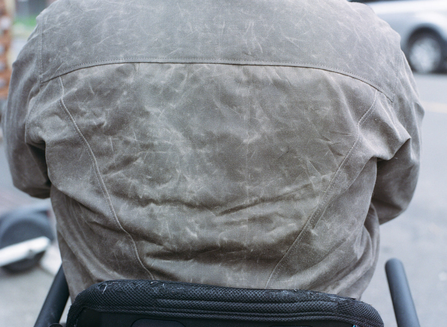 The back of a brown waxed canvas jacket worn by a man in a wheelchair.