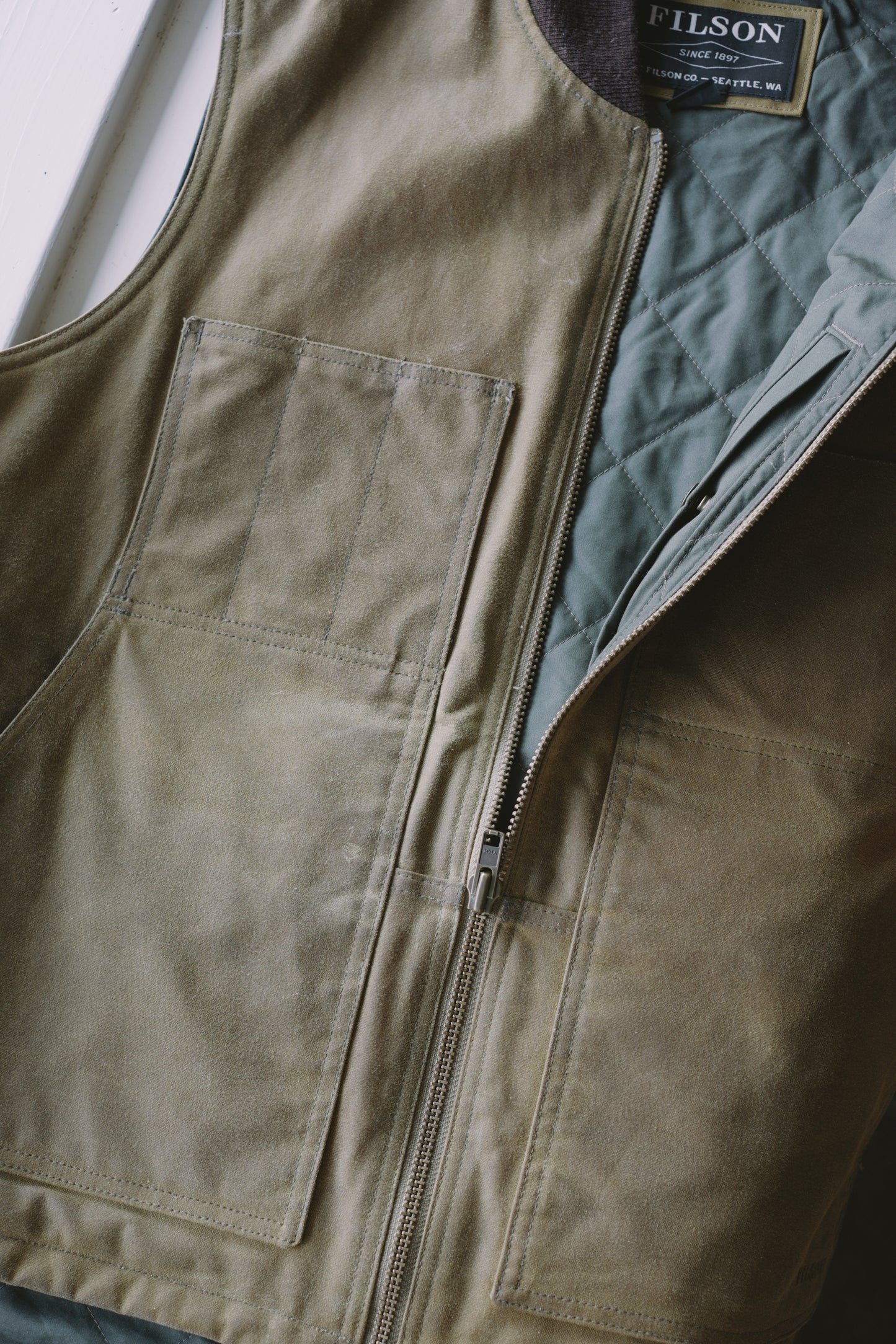 An image of a Filson waxed canvas tin cloth vest, with diamond pattern insulation.