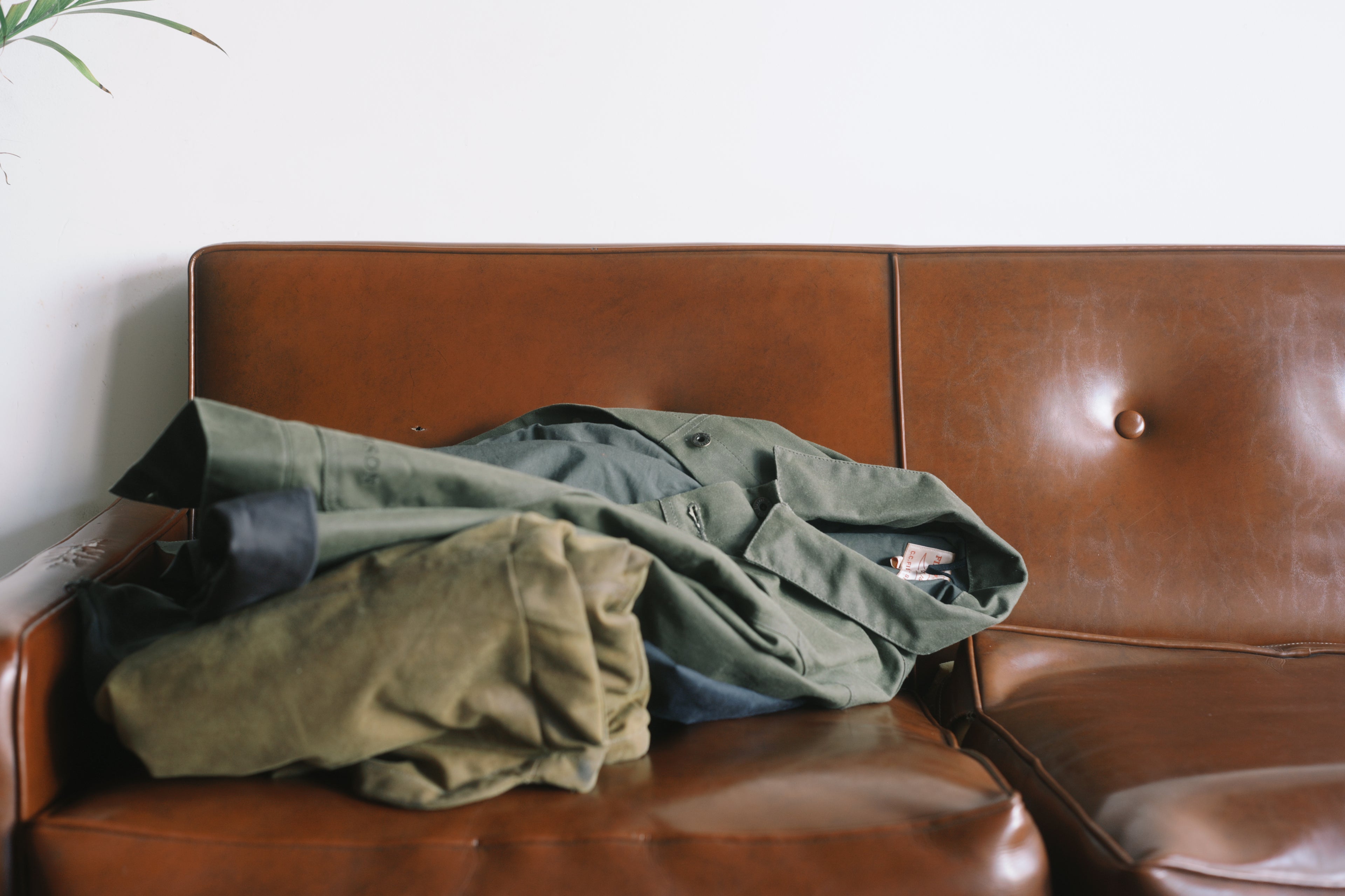 An image of waxed canvas jackets resting on a brown leather couch.