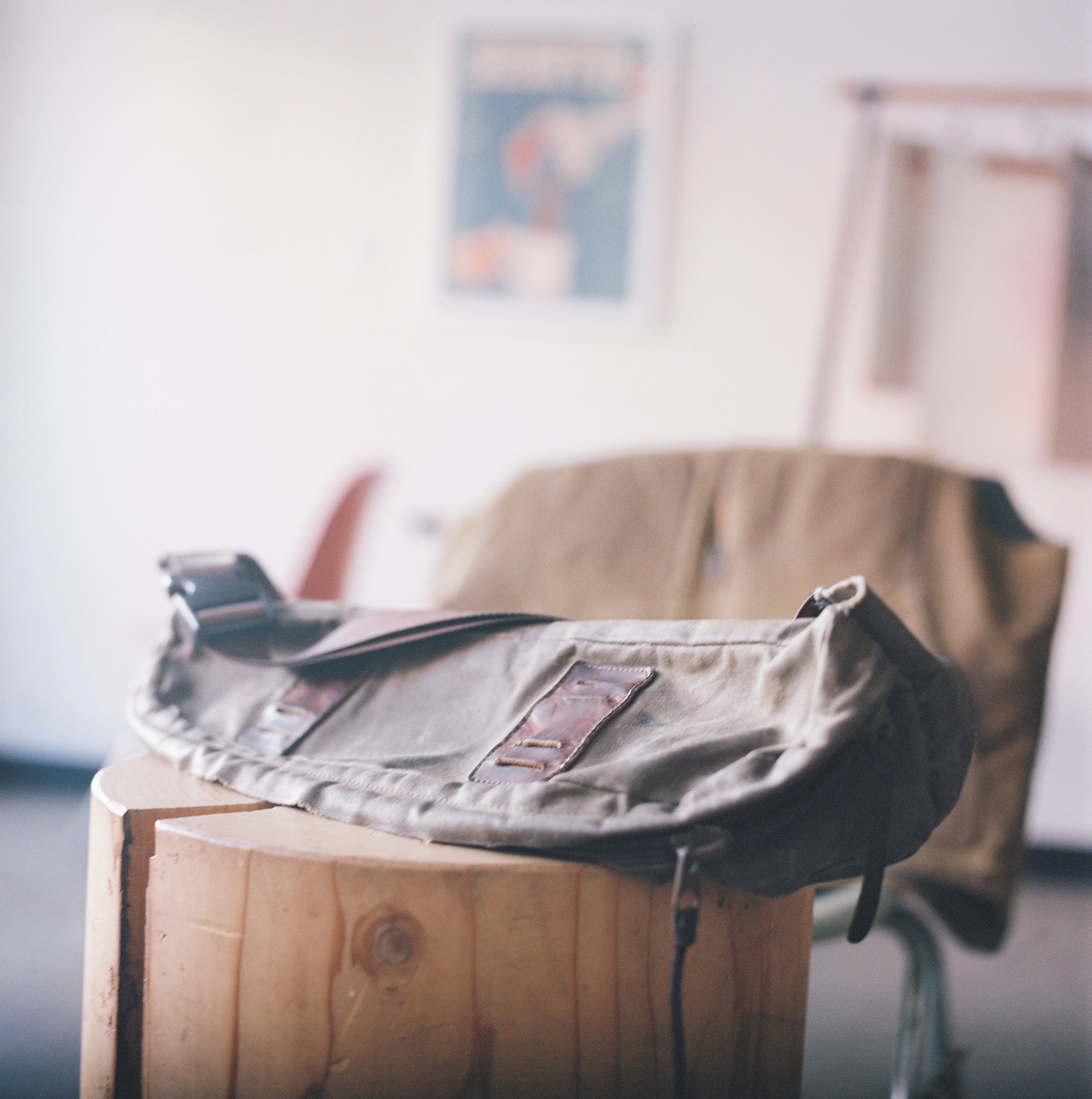 An image of a handmade waxed canvas sling bag resting on a wooden stump table. 